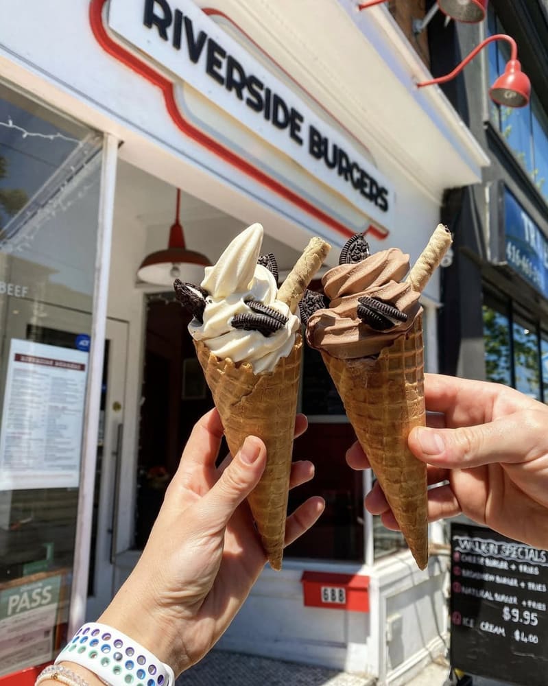Two ice cream cones held up in front of the Riverside Burgers storefront